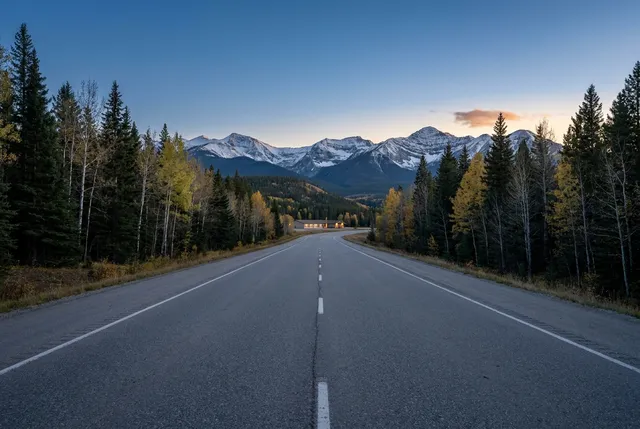 Two-lane highway through spruce and aspen toward the Rockies at dusk
